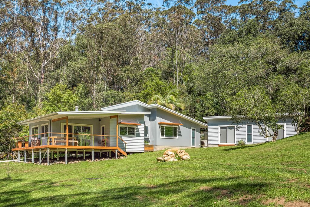 Custom-designed energy-efficient home with a spacious deck, surrounded by lush greenery, showcasing Living Green Designer Homes' commitment to quality and client satisfaction.