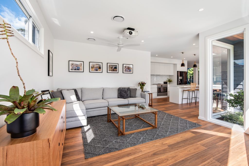 Modern living room featuring a comfortable gray sectional sofa, wooden coffee table, and natural light from large windows, emphasizing sustainable home design aesthetics.
