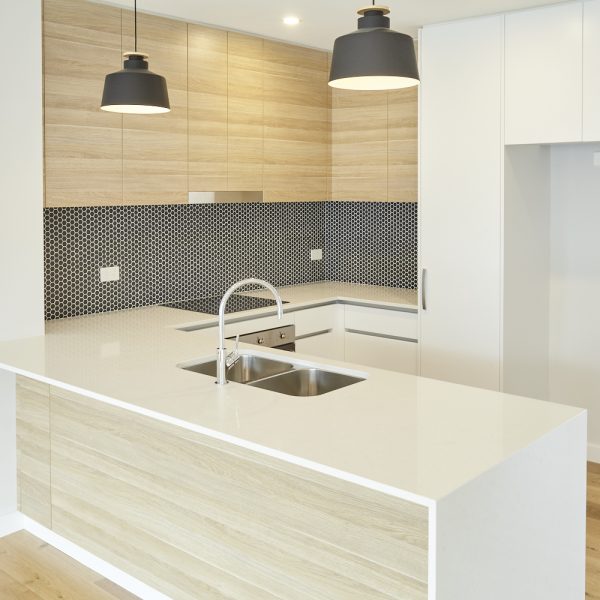 Modern kitchen design featuring sleek cabinetry, a white stone countertop, stainless steel sink, and contemporary pendant lighting, highlighting the premium finishes of the Seabreeze housing development by Living Green Designer Homes.