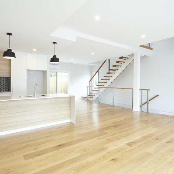 Spacious interior of a modern environmentally friendly home featuring a kitchen island, wooden flooring, and a staircase, part of the Seabreeze housing development by Living Green Designer Homes.