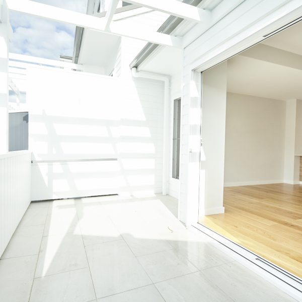 Bright, airy outdoor patio leading to modern interior space with wooden flooring, showcasing the sustainable design of the Seabreeze housing development by Living Green Designer Homes.