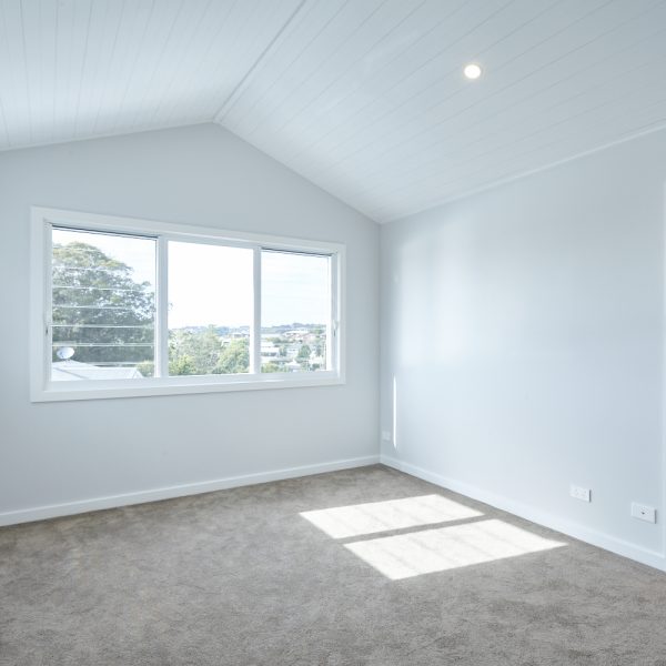 Bright interior of a modern bedroom in the Seabreeze housing development by Living Green Designer Homes, featuring a large window with scenic views, high ceilings, and neutral-colored walls.