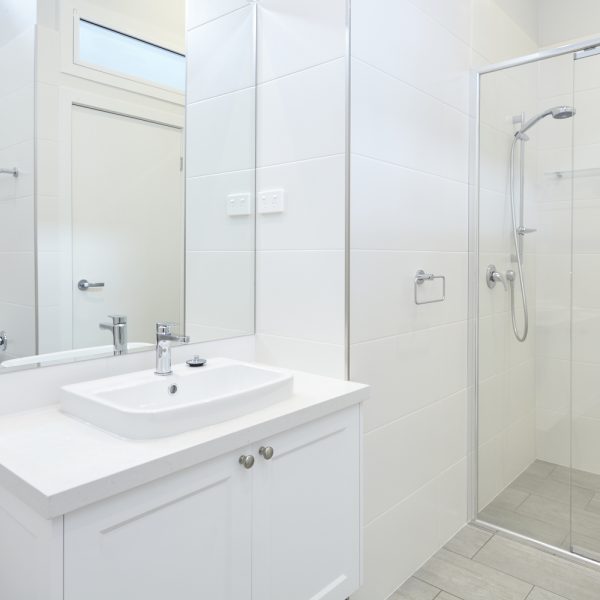 Modern bathroom design featuring a sleek white vanity with a rectangular sink, polished chrome faucet, and large mirror, alongside a glass shower enclosure with a minimalist aesthetic, emphasizing the sustainable and premium finishes of the Seabreeze housing development.