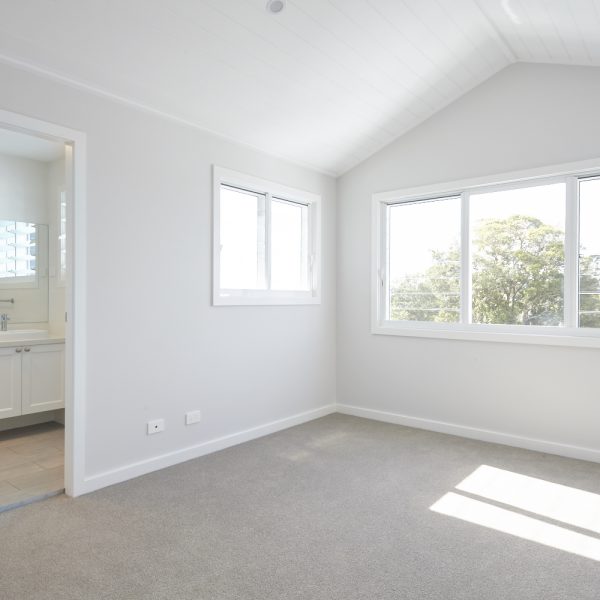 Bright and airy interior of a modern bedroom featuring large windows, soft carpeting, and a view of greenery, showcasing the design aesthetics of the Seabreeze housing development by Living Green Designer Homes.