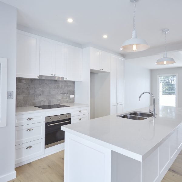 Modern kitchen featuring white cabinetry, stainless steel appliances, and a large island with a sink, showcasing the design and premium finishes of the Seabreeze housing development by Living Green Designer Homes.