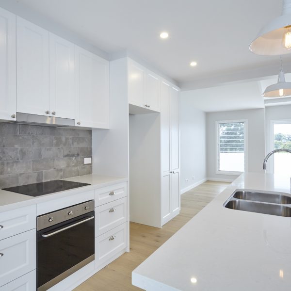 Modern kitchen interior featuring white cabinetry, sleek countertops, stainless steel appliances, and a large window providing natural light, highlighting the eco-friendly design of the Seabreeze housing development by Living Green Designer Homes.