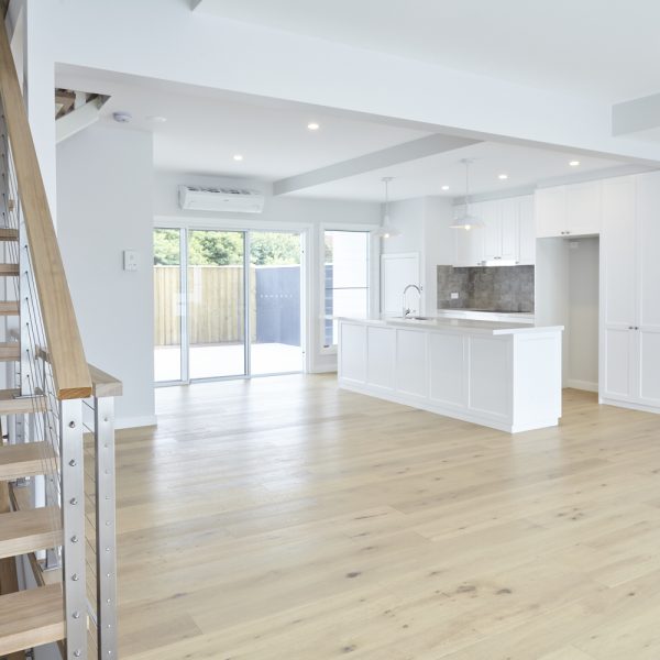 Modern open-plan living space in Seabreeze housing development, featuring light wood flooring, white cabinetry, and large windows for natural light.