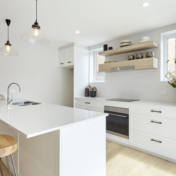 Modern kitchen design featuring white cabinetry, a central island with a sink, minimalist decor, and natural light from windows, showcasing environmentally friendly features in the Seabreeze housing development by Living Green Designer Homes.