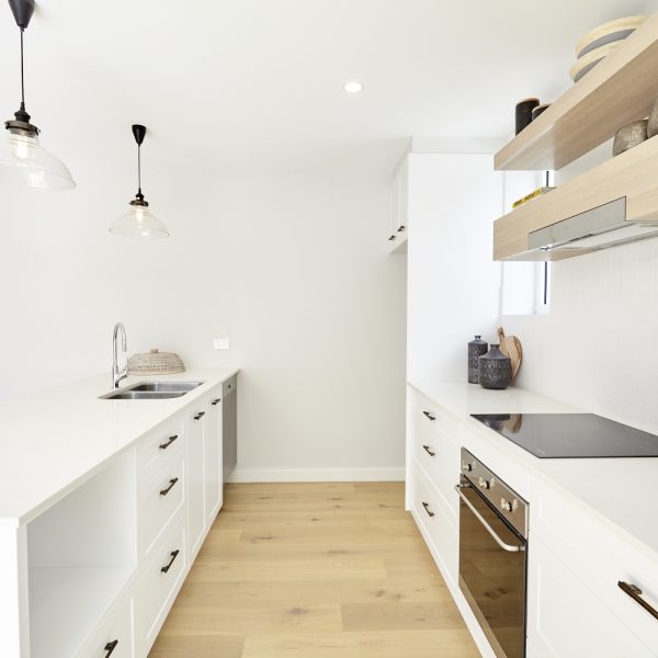 Modern kitchen interior featuring white cabinetry, stainless steel appliances, and wooden flooring, highlighting eco-friendly design elements from the Seabreeze project by Living Green Designer Homes.