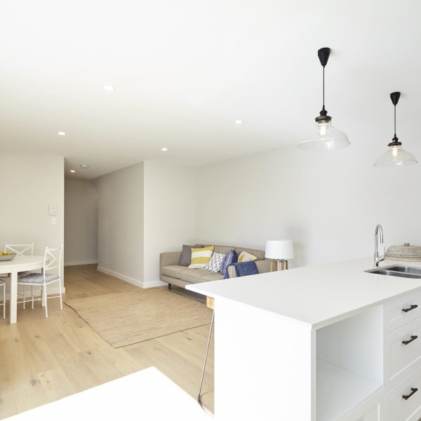 Modern interior of Seabreeze housing development featuring open-plan living area with stylish sofa, dining table, and pendant lighting, emphasizing sustainable design by Living Green Designer Homes.