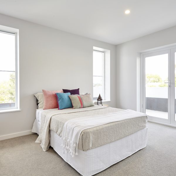 Modern bedroom in Seabreeze housing development featuring a bed with decorative pillows, natural light from large windows, and minimalist design elements.
