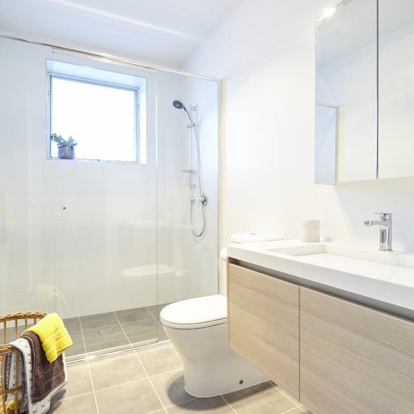 Modern bathroom design featuring a glass shower enclosure, sleek vanity with storage, and natural light from a window, showcasing environmentally friendly finishes in the Seabreeze housing development by Living Green Designer Homes.