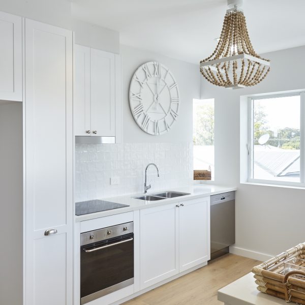 Modern kitchen design featuring white cabinetry, stainless steel appliances, and a decorative clock, showcasing the stylish and sustainable features of the Seabreeze project by Living Green Designer Homes.