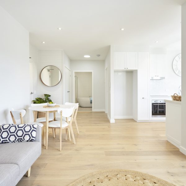 Modern interior of a sustainable home featuring a dining area with a round table, white chairs, and a cozy sofa, showcasing eco-friendly design elements and premium finishes in the Seabreeze project by Living Green Designer Homes.