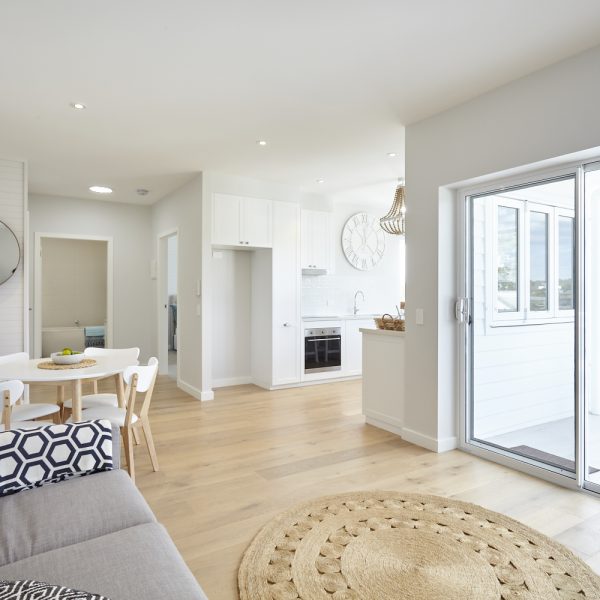 Modern open-plan living space in Seabreeze housing development by Living Green Designer Homes, featuring stylish kitchen, dining area, and natural light from sliding door.