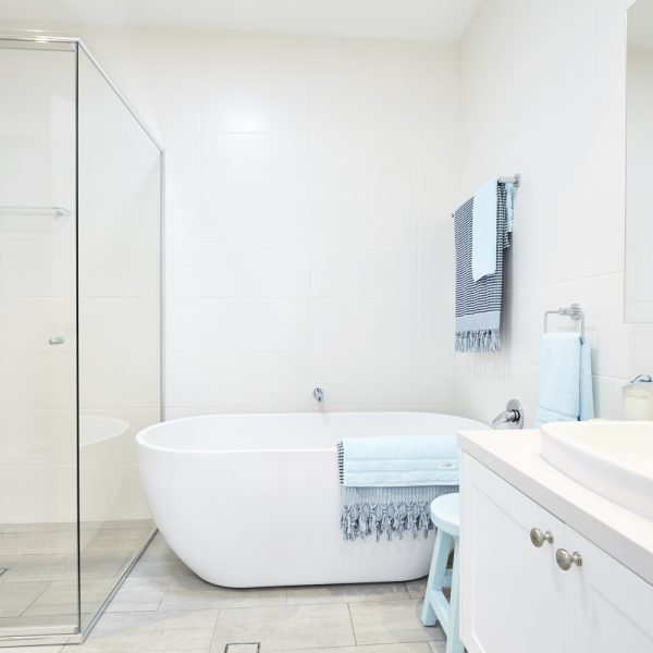 Modern bathroom featuring a freestanding white bathtub, glass shower enclosure, and light blue accents, showcasing eco-friendly design elements in the Seabreeze housing development by Living Green Designer Homes.