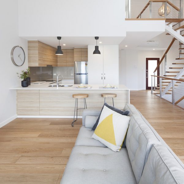 Modern interior of the Seabreeze housing development by Living Green Designer Homes, featuring a stylish kitchen with wooden cabinetry, a kitchen island with seating, and a cozy living area with a decorative pillow, emphasizing sustainable design and premium finishes.