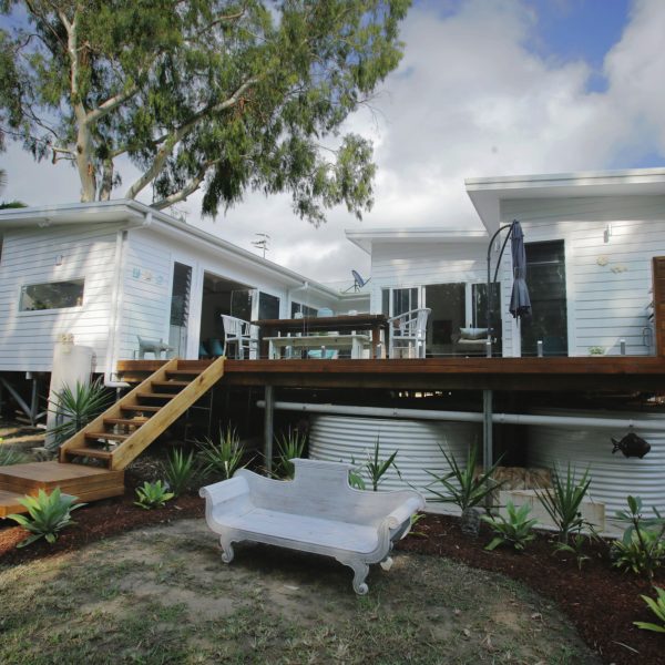 Family-friendly sustainable home design featuring wooden deck, outdoor dining area, and landscaped garden with seating, emphasizing energy efficiency and functionality.