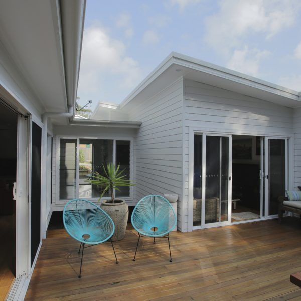 Family-friendly outdoor deck with turquoise chairs, potted plant, and modern home design, showcasing sustainable living features by Living Green Designer Homes.