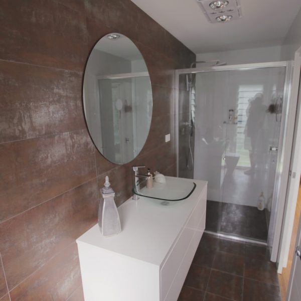 Modern bathroom design featuring a round mirror, sleek white vanity, and glass shower enclosure, emphasizing sustainable and family-friendly aesthetics.