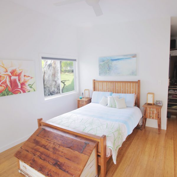 Brightly lit bedroom featuring a wooden bed with a blue and green comforter, decorative pillows, and artwork on the walls, emphasizing family-friendly and sustainable design elements.