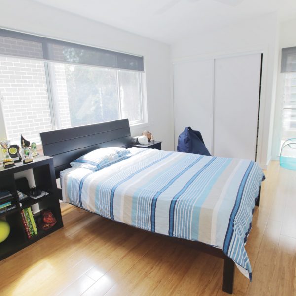 Modern family-friendly bedroom with a striped blue and white bedspread, wooden flooring, and natural light from large windows, reflecting the design ethos of Living Green Designer Homes.