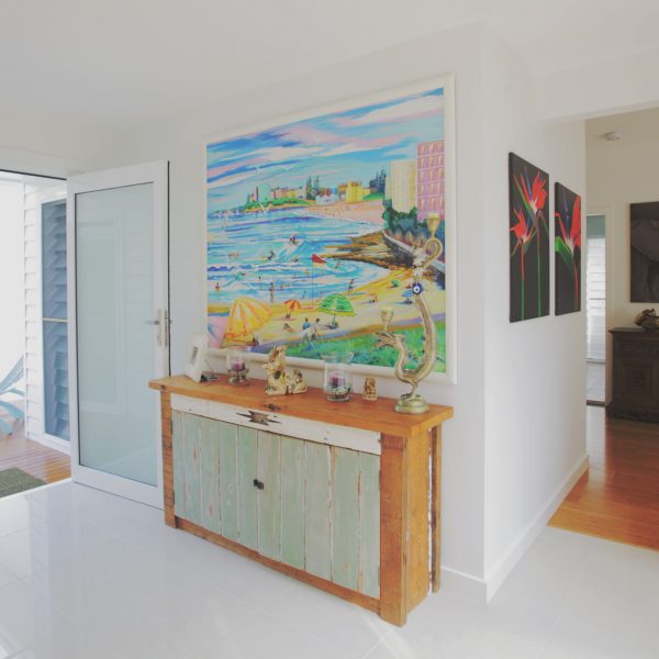 Bright entryway featuring a wooden console table with decorative items, a colorful beach painting on the wall, and modern artwork, emphasizing family-friendly and sustainable home design.