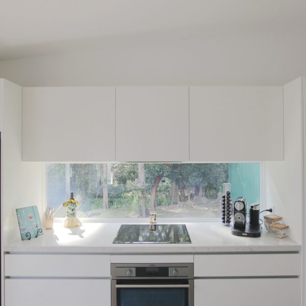 Modern kitchen with white cabinetry, marble countertop, and energy-efficient appliances, featuring a large window overlooking greenery, emphasizing family-friendly design and sustainability.