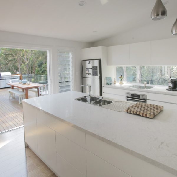 Modern kitchen design with white cabinetry, marble countertop, and stainless steel appliances, featuring a view of a deck and outdoor dining area, highlighting family-friendly and sustainable living.