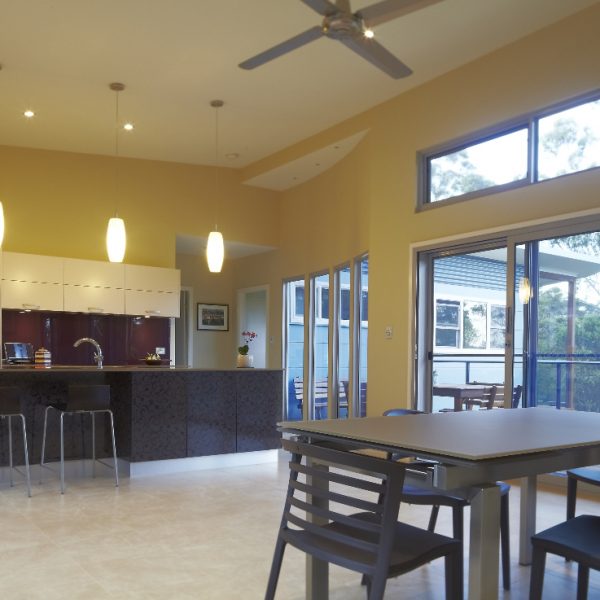 Modern kitchen and dining area in sustainable home, featuring sleek cabinetry, pendant lighting, and large windows with natural light, emphasizing eco-friendly design elements.