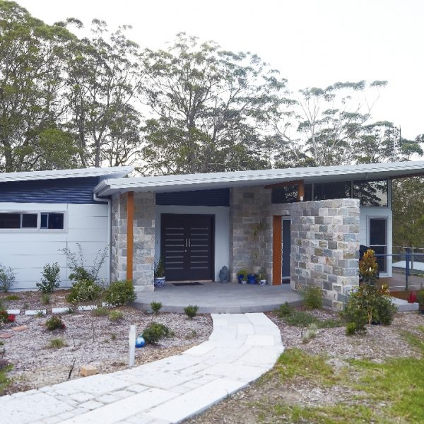 Modern eco-friendly home design featuring natural stone facade, landscaped garden, and inviting entrance, part of Living Green Designer Homes' sustainable architecture portfolio.