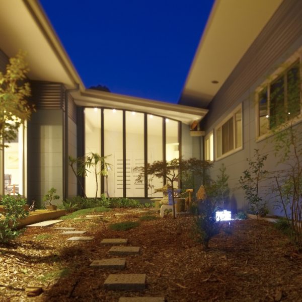 Hilltop Hideaway home featuring a central Japanese-style garden, modern architecture, and energy-efficient design elements, illuminated at dusk.