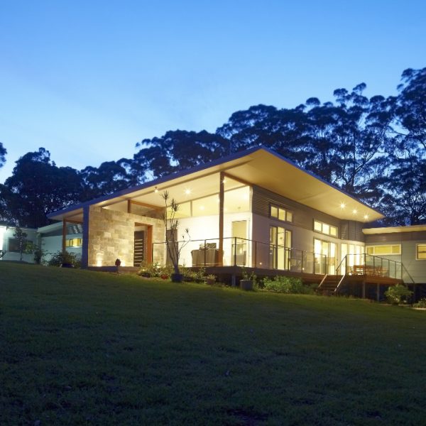 Sustainable eco-home 'Hilltop Hideaway' by Living Green Designer Homes, featuring modern design, large windows, and a landscaped garden at dusk.