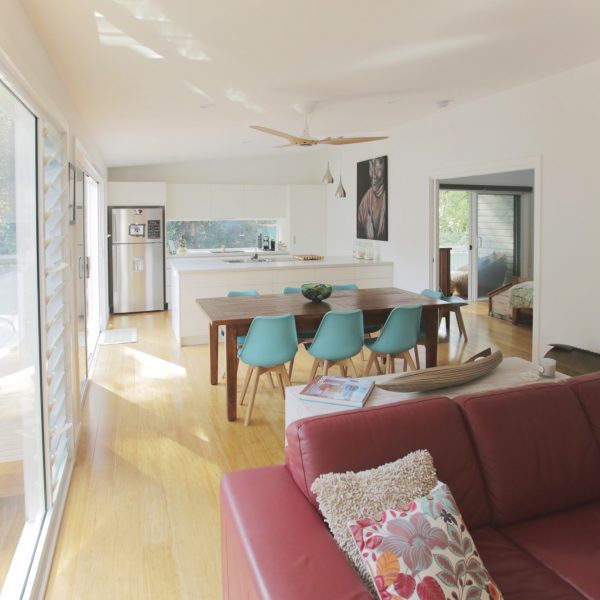 Modern family-friendly kitchen and dining area featuring wooden dining table with turquoise chairs, sleek white cabinetry, and natural light, emphasizing sustainable design by Living Green Designer Homes.