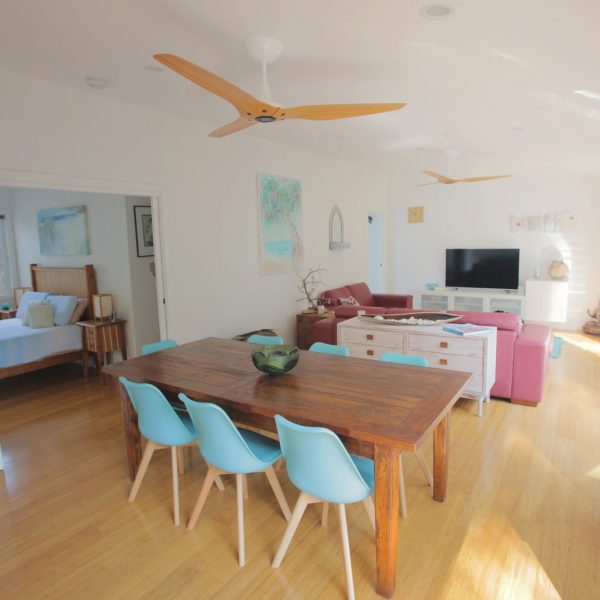 Family-friendly living space featuring a wooden dining table with light blue chairs, modern decor, and sustainable design elements, showcasing a cozy lounge area with a TV and natural light.