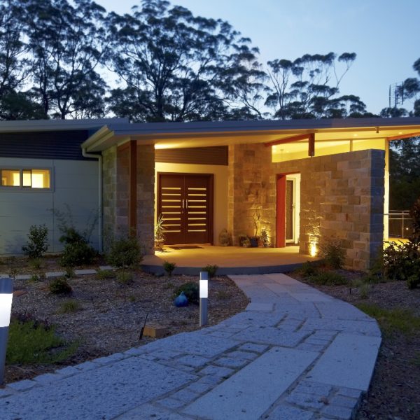 Hilltop Hideaway home entrance featuring modern architecture, stone façade, wooden doors, and landscaped pathway illuminated by outdoor lighting.