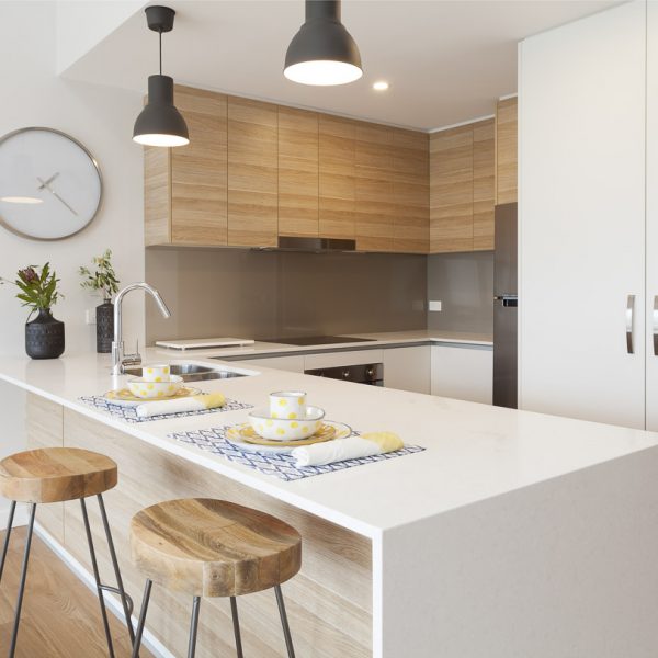 Modern kitchen with wooden cabinetry, white stone countertop, and stylish bar stools, featuring tableware with yellow polka dots, emphasizing the sustainable design of the Seabreeze project by Living Green Designer Homes.