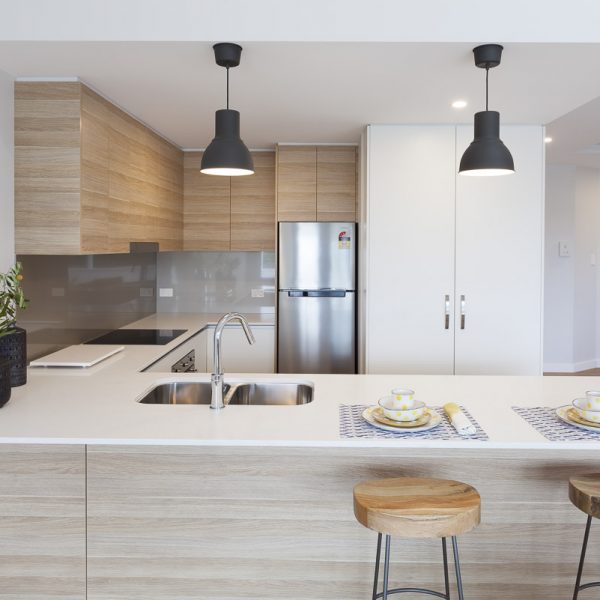 Modern kitchen design featuring light wood cabinetry, stainless steel appliances, double sink, and minimalist decor, showcasing eco-friendly elements in the Seabreeze project by Living Green Designer Homes.