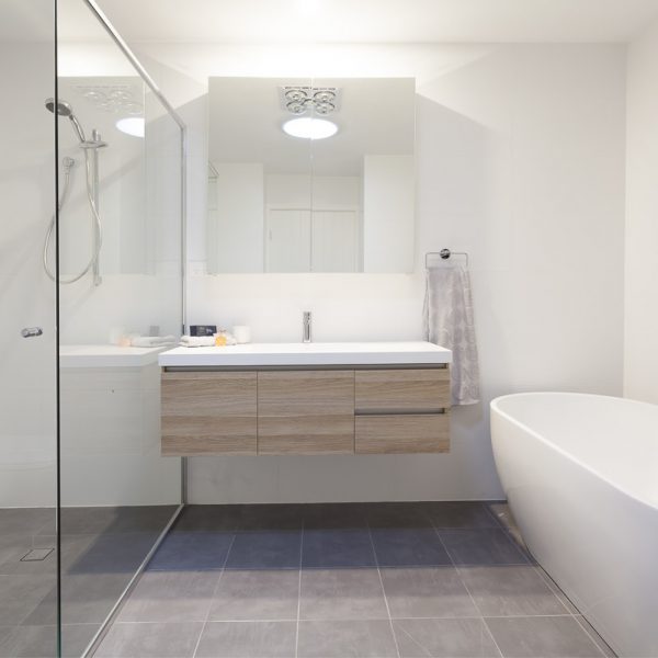 Modern bathroom design featuring a sleek vanity with wooden cabinetry, a large mirror, a glass shower enclosure, and a freestanding bathtub, emphasizing sustainability and premium finishes by Living Green Designer Homes.