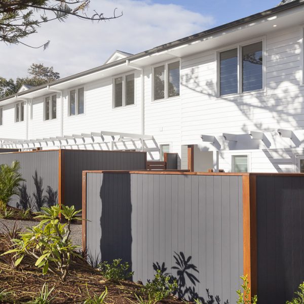 Modern environmentally friendly home exterior with white siding, large windows, and landscaped garden featuring grey fencing and tropical plants, part of the Seabreeze project by Living Green Designer Homes.