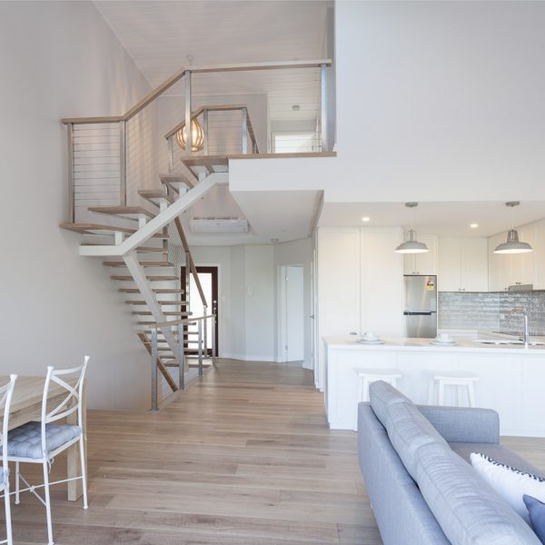 Modern interior of a sustainable home featuring open-plan living area, stylish kitchen with premium finishes, wooden flooring, and a staircase leading to an upper level.