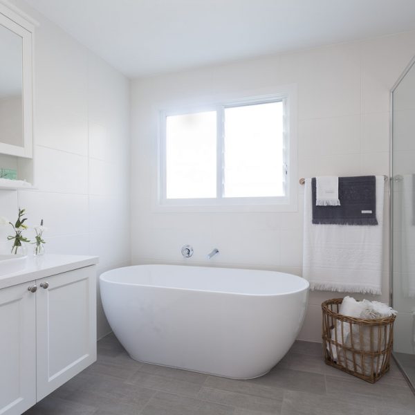 Modern bathroom featuring a freestanding white bathtub, natural light from a window, and stylish finishes, reflecting the sustainable design ethos of the Seabreeze project by Living Green Designer Homes.
