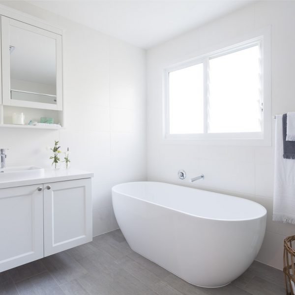 Modern bathroom featuring a freestanding white bathtub, sleek cabinetry, and natural light from a window, showcasing the elegant design of the Seabreeze housing development by Living Green Designer Homes.