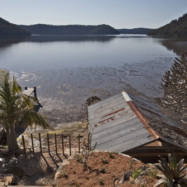 Scenic view of a tranquil river with a weathered shed, lush greenery, and a wooden pier, highlighting sustainable living and natural surroundings.