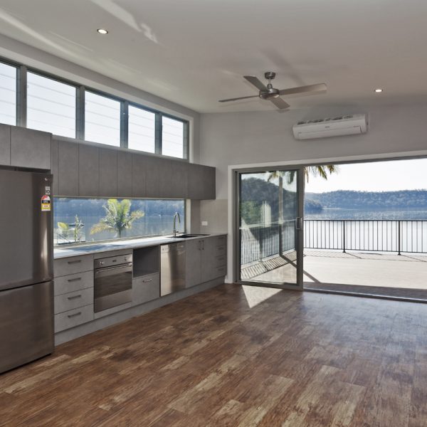 Modern kitchen interior with sleek cabinetry, stainless steel appliances, and large windows showcasing a scenic river view, emphasizing sustainable design by Living Green Designer Homes.