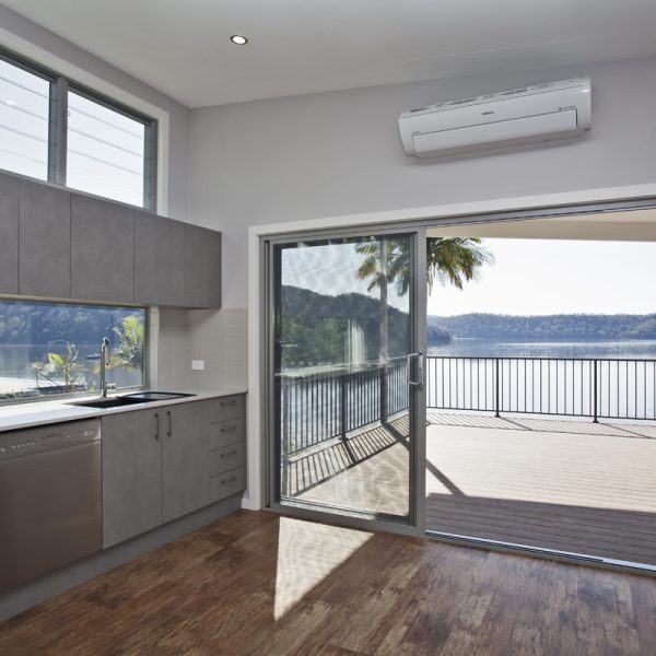 Modern kitchen with gray cabinetry, stainless steel appliances, and a view of the river through sliding glass doors, showcasing sustainable design elements and indoor-outdoor living.