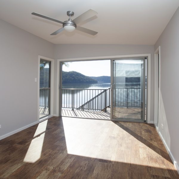 Spacious living area with panoramic lake views, featuring large sliding doors, wooden flooring, and a ceiling fan, highlighting sustainable design elements of River View Homes by Living Green Designer Homes.