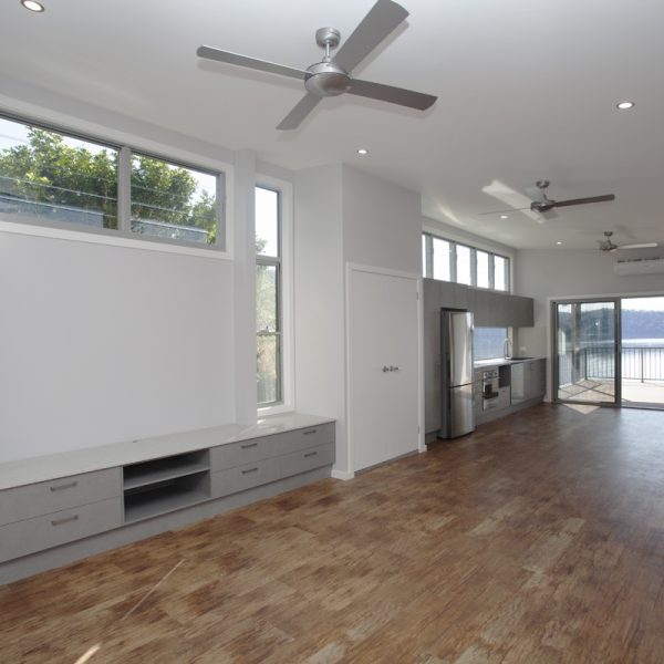 Modern open-plan living space featuring large windows, wooden flooring, and a sleek kitchen area, showcasing sustainable design elements by Living Green Designer Homes.