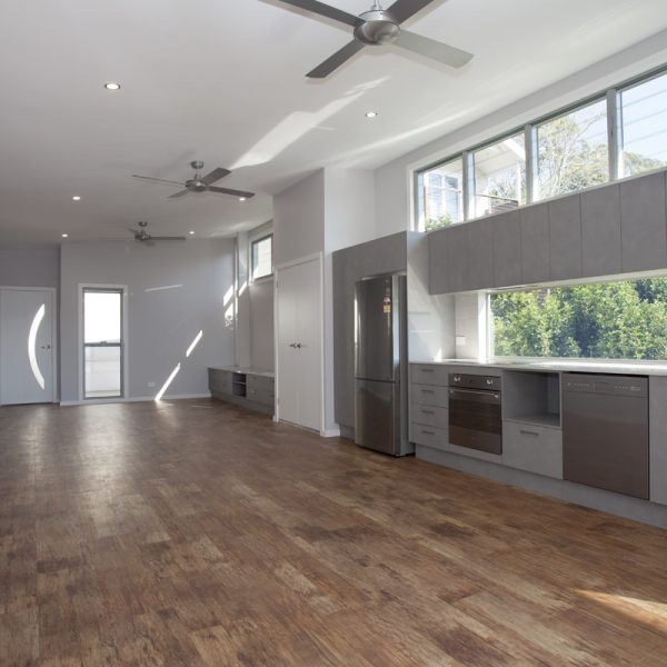 Spacious modern kitchen and living area showcasing sustainable design elements, featuring large windows, wooden flooring, and stainless steel appliances, highlighting Living Green Designer Homes' innovative construction techniques.