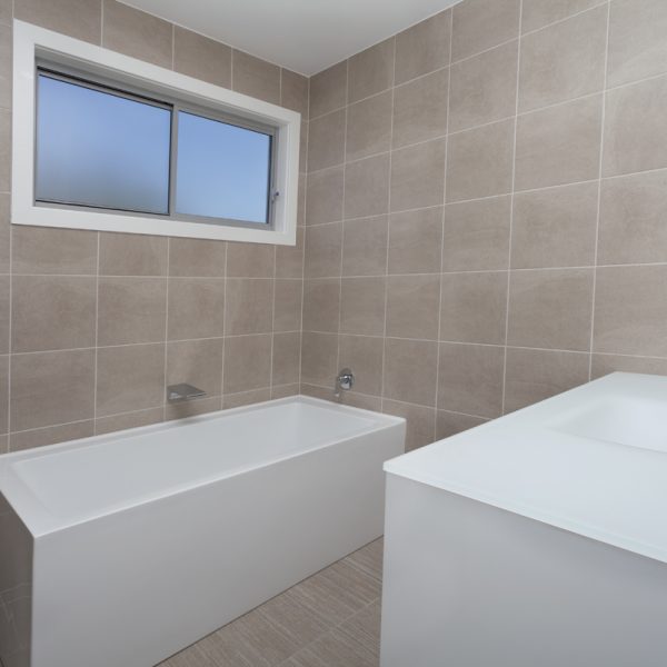 Modern bathroom design featuring a white bathtub, minimalist sink, and neutral tiled walls, showcasing sustainable construction elements by Living Green Designer Homes.